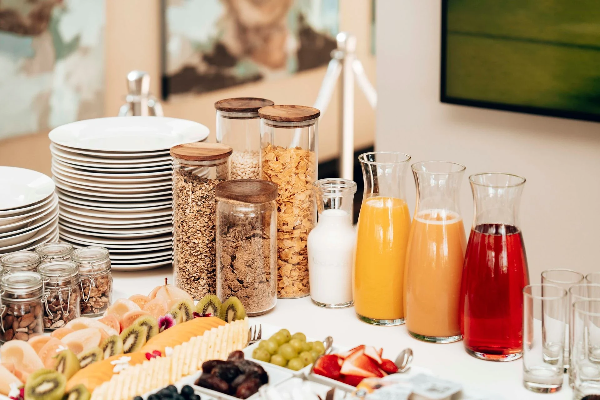 A self-service breakfast station with cereals, sliced fruit, juice and stacked plates