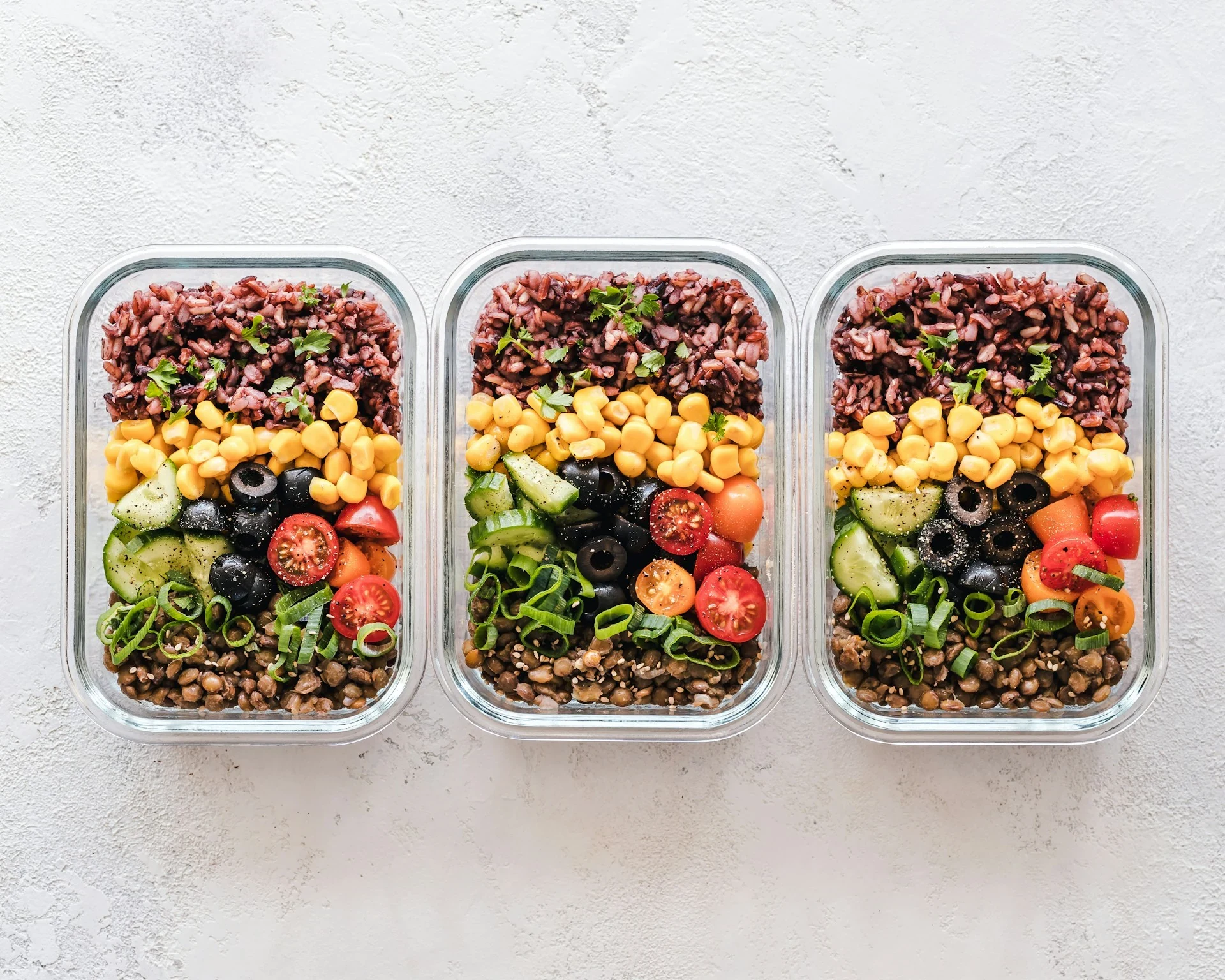 Three glass meal containers packed with rice, lentils, corn and vegetables